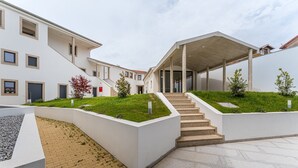 Un edificio moderno con una escalera cubierta, techo plano y un área ajardinada con césped y plantas.