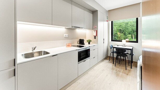 Una cocina moderna con horno integrado, un lavamanos y una zona de comedor con mesa y sillas.
