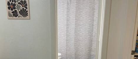 Una habitación con una mesa de madera, un tapete estampado, una cortina de ducha y una obra de arte en la pared.