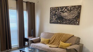 A living room with a sofa, a coffee table, a patterned rug, and a ceiling fan. - The Peacock Pad Retro-Vibe, Newly Renovated 2 bed Duplex, Hourglass-Sodo area (Orlando)