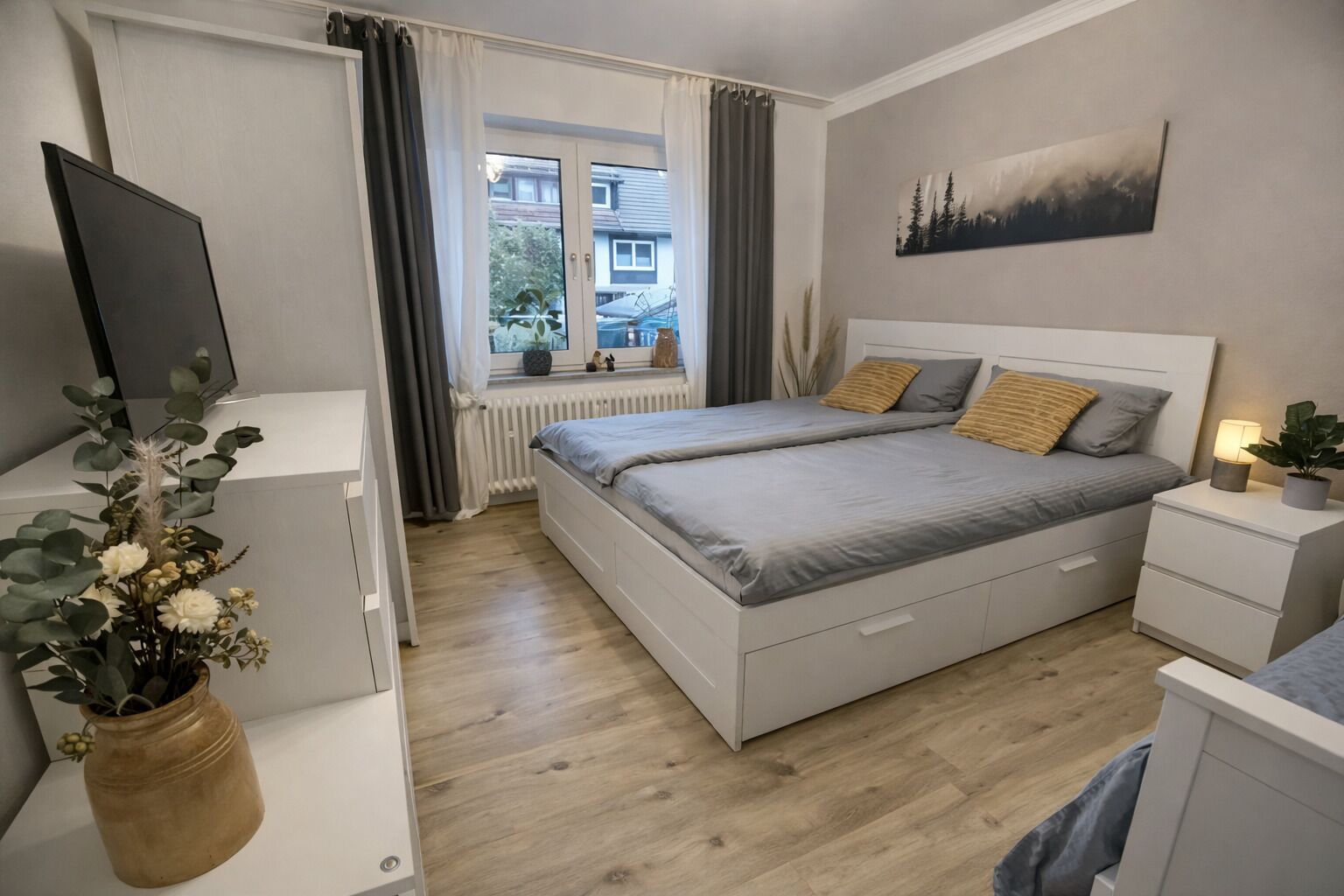 A bedroom with a bed, bedside tables, a TV, and a window with curtains.