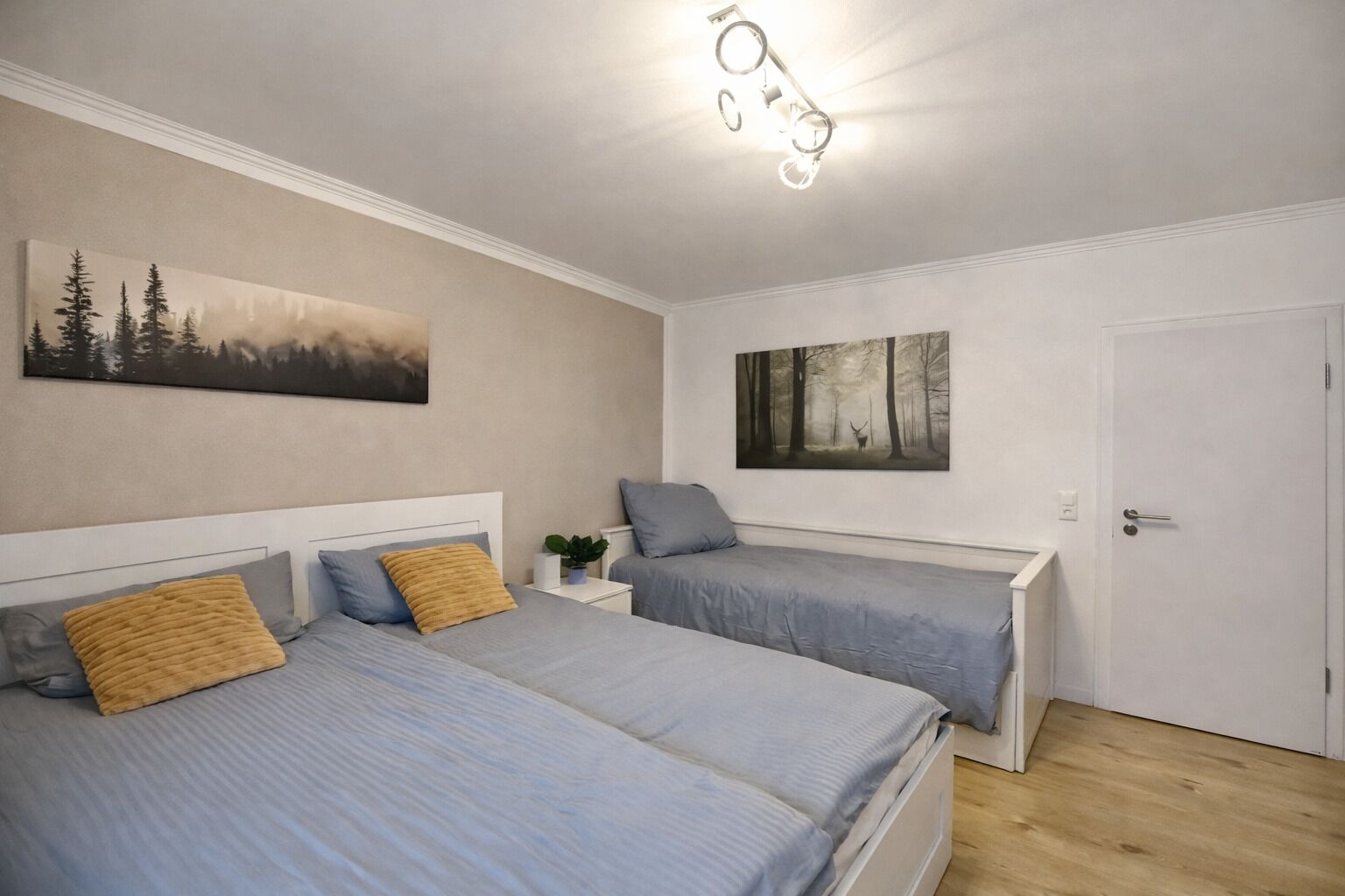 A bedroom with two beds, a nightstand, a wall-mounted light fixture, and two paintings.
