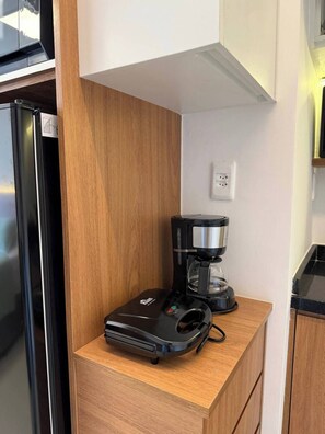 A compact kitchen with a coffee maker, a refrigerator, and a wooden cabinet. - Studio Cristo Redentor (Rio de Janeiro)