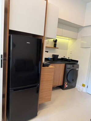 A compact kitchen with a black refrigerator, a washing machine, and a stove. - Studio Cristo Redentor (Rio de Janeiro)