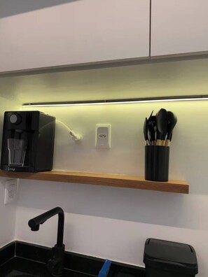 A kitchen with a coffee machine, a power outlet, and a utensil holder on a shelf. - Studio Cristo Redentor (Rio de Janeiro)