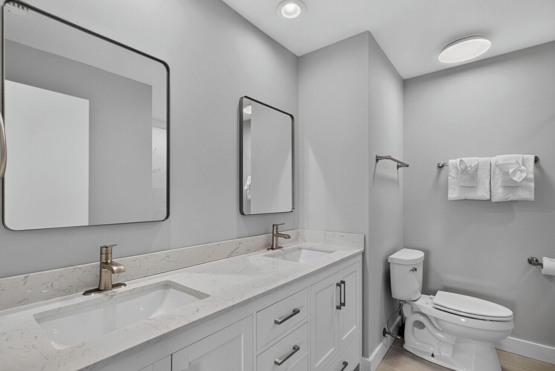 A modern bathroom with two sinks, a toilet, and a mirror.
