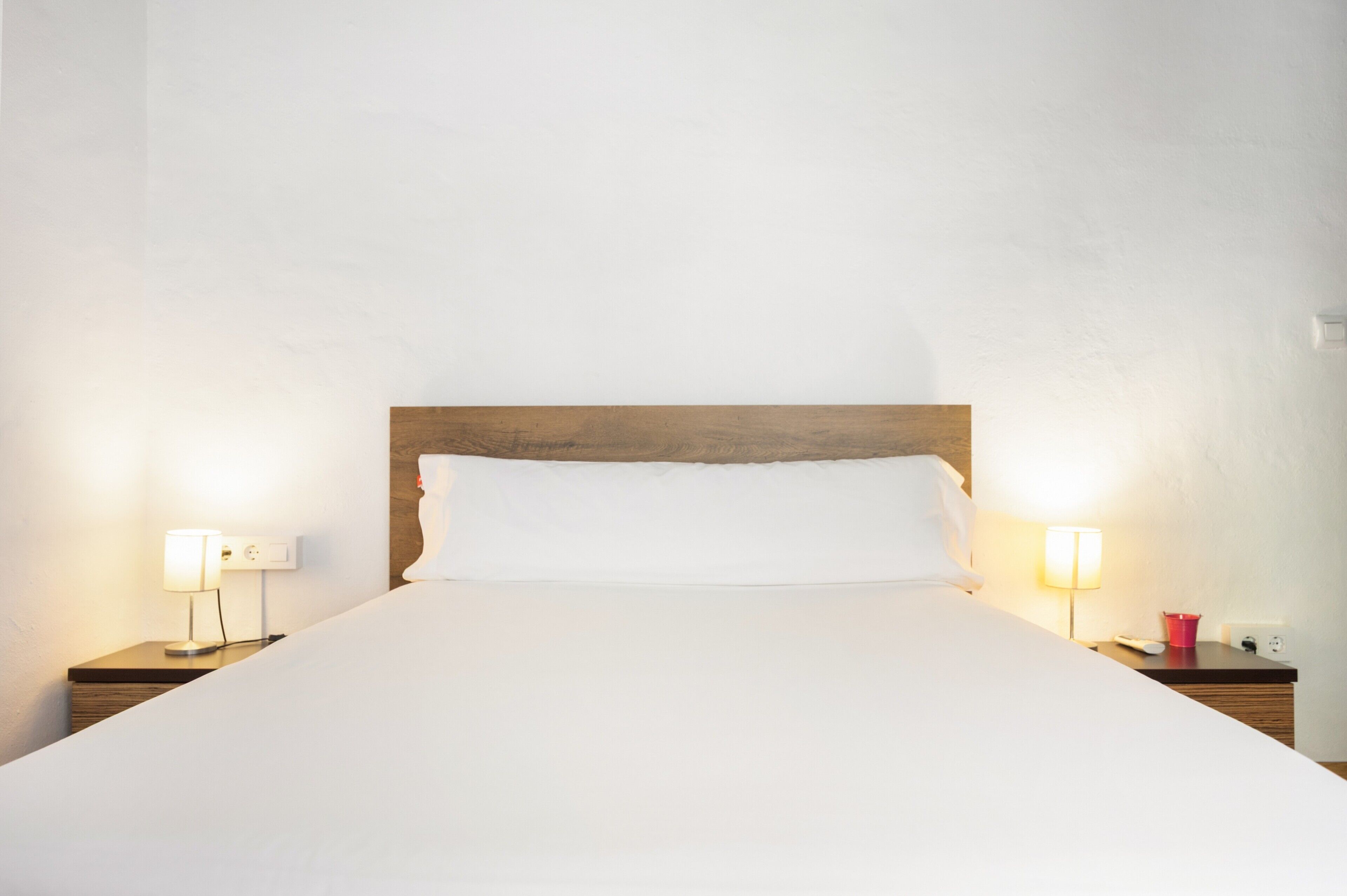 Un letto con lenzuola bianche, una testiera in legno e due lampade sui comodini.