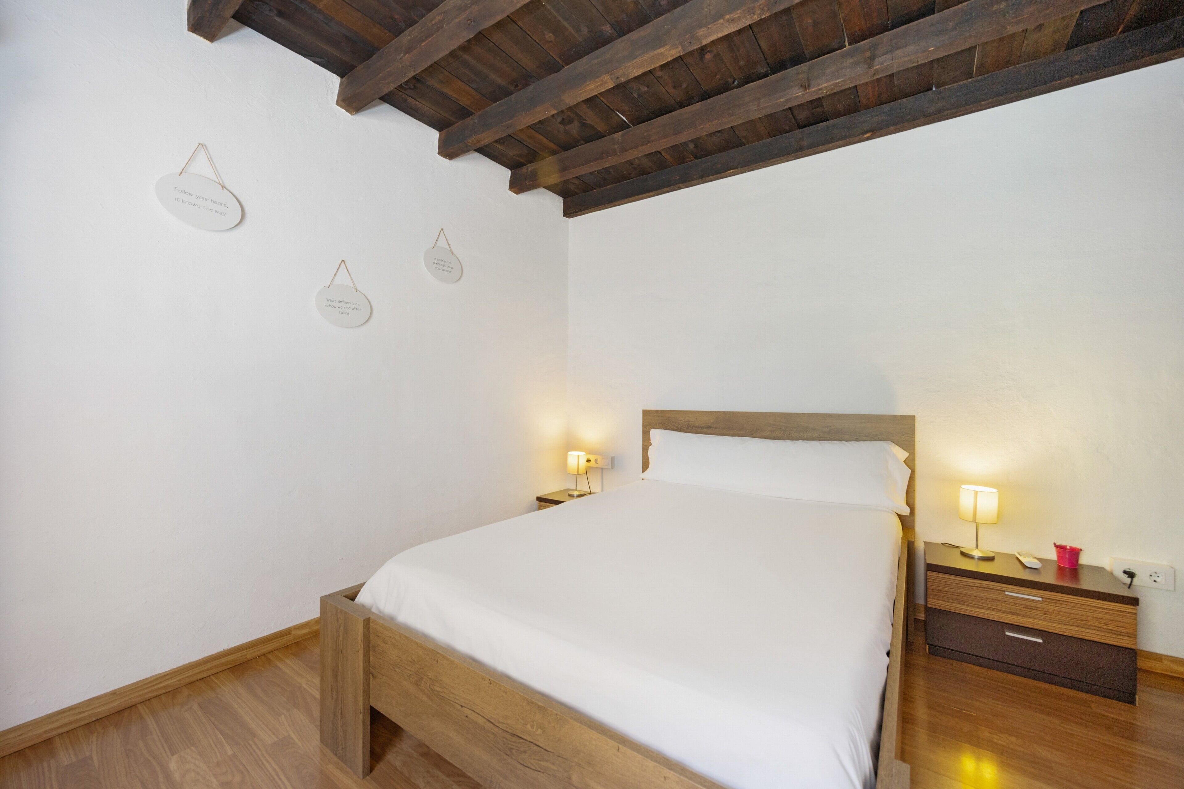 Un dormitorio con cama de madera, mesitas de noche con lámparas e iluminación en la pared.