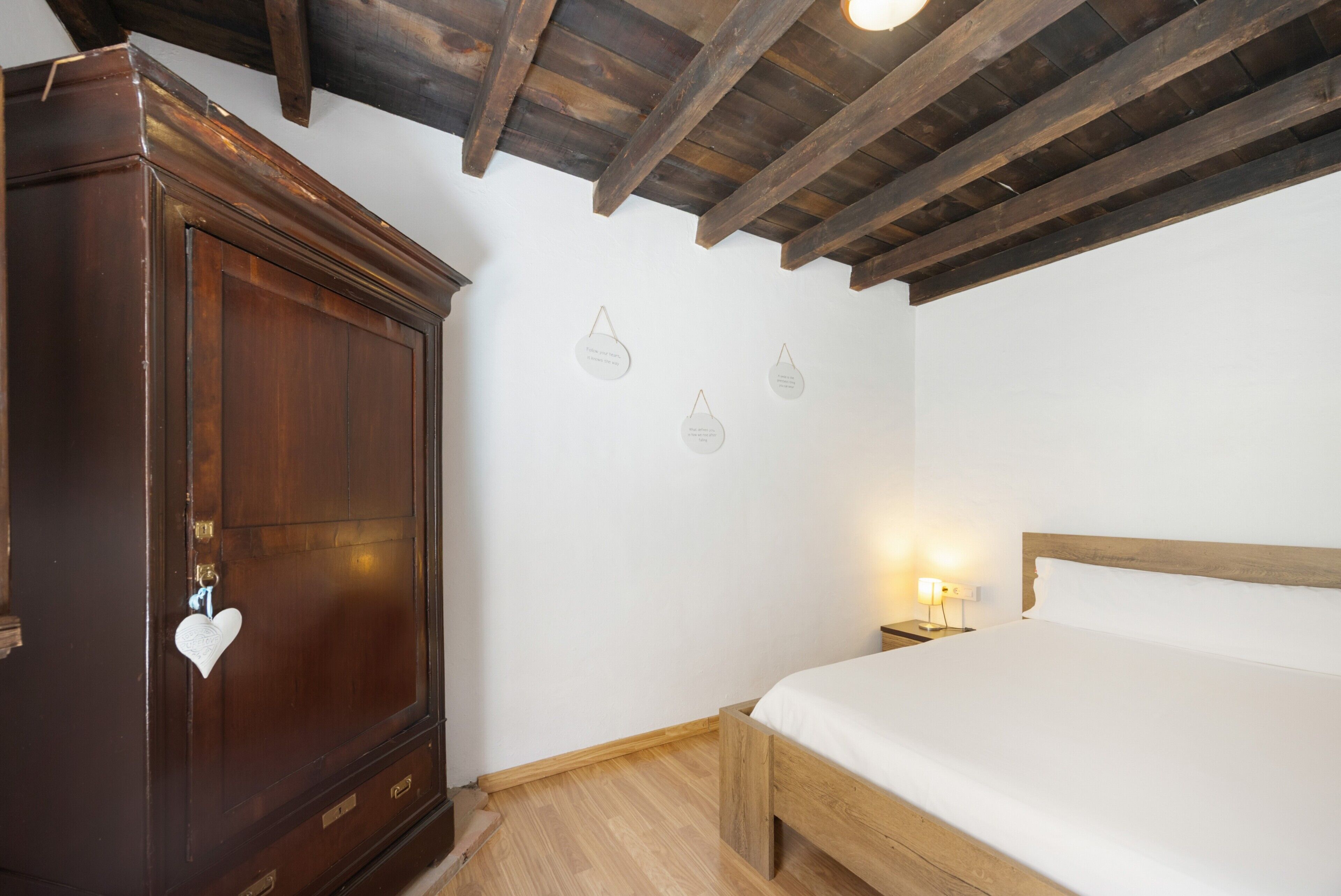 Une chambre à coucher avec une armoire en bois, un lit et une table de chevet avec une lampe.
