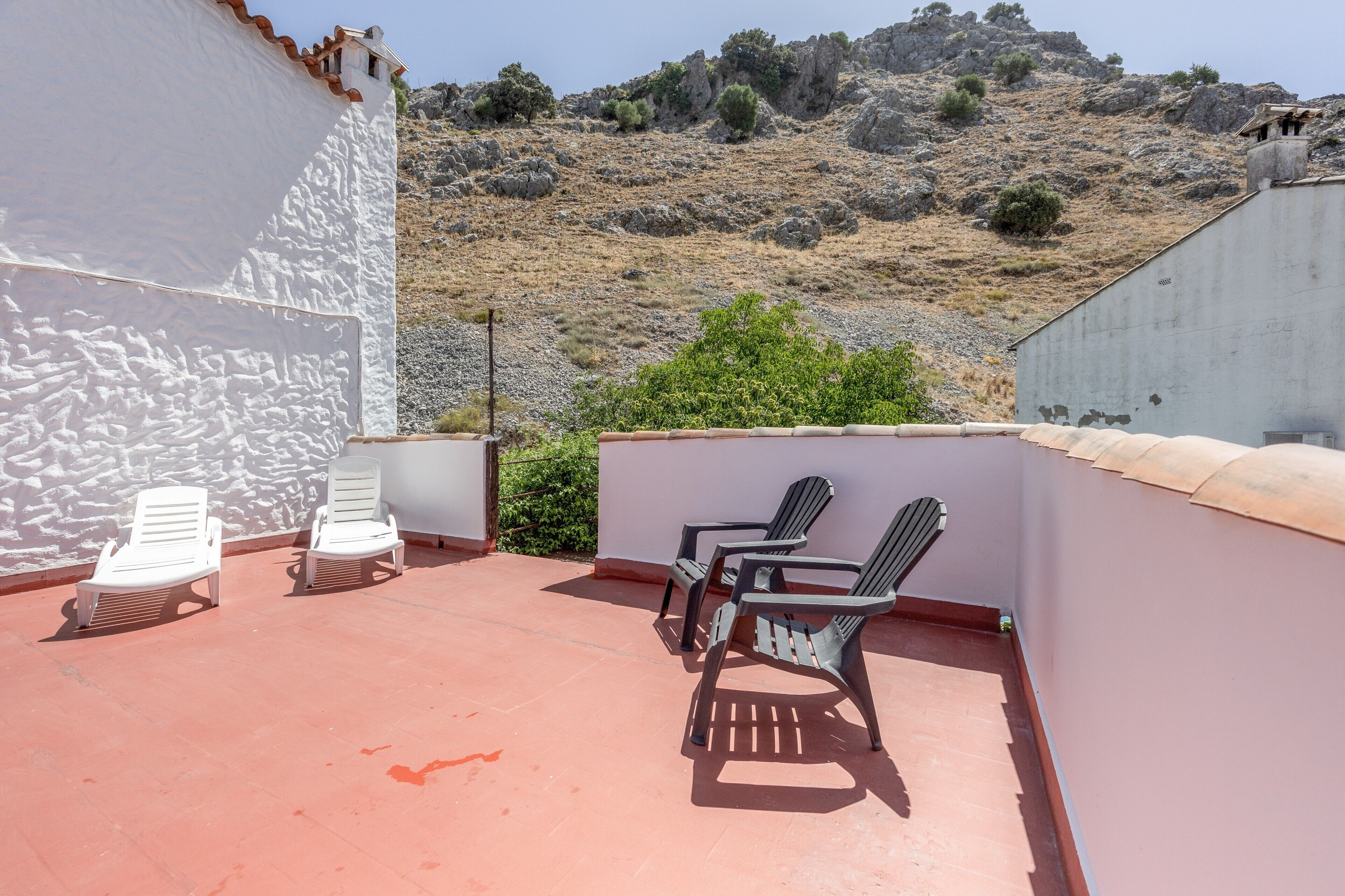 Una terraza en la azotea con sillones de descanso blancos y negros, un muro de hormigón y vistas a una ladera rocosa.