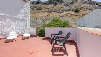 Una terraza en la azotea con sillones de descanso blancos y negros, un muro de hormigón y vistas a una ladera rocosa.