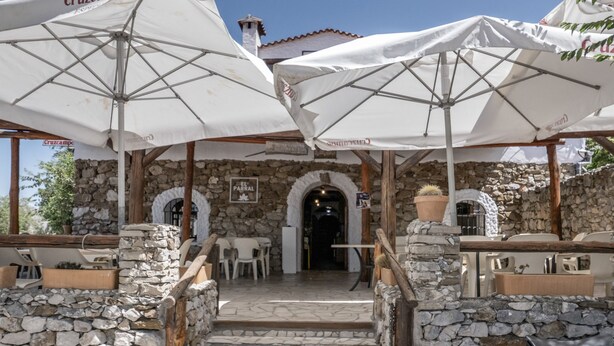 Outdoor seating with umbrellas, stone walls, and a stone staircase leading to an entrance. - Hostal Posada El Parral – Private Pool and Restaurant in the Sierra de Cádiz (Benaocaz)