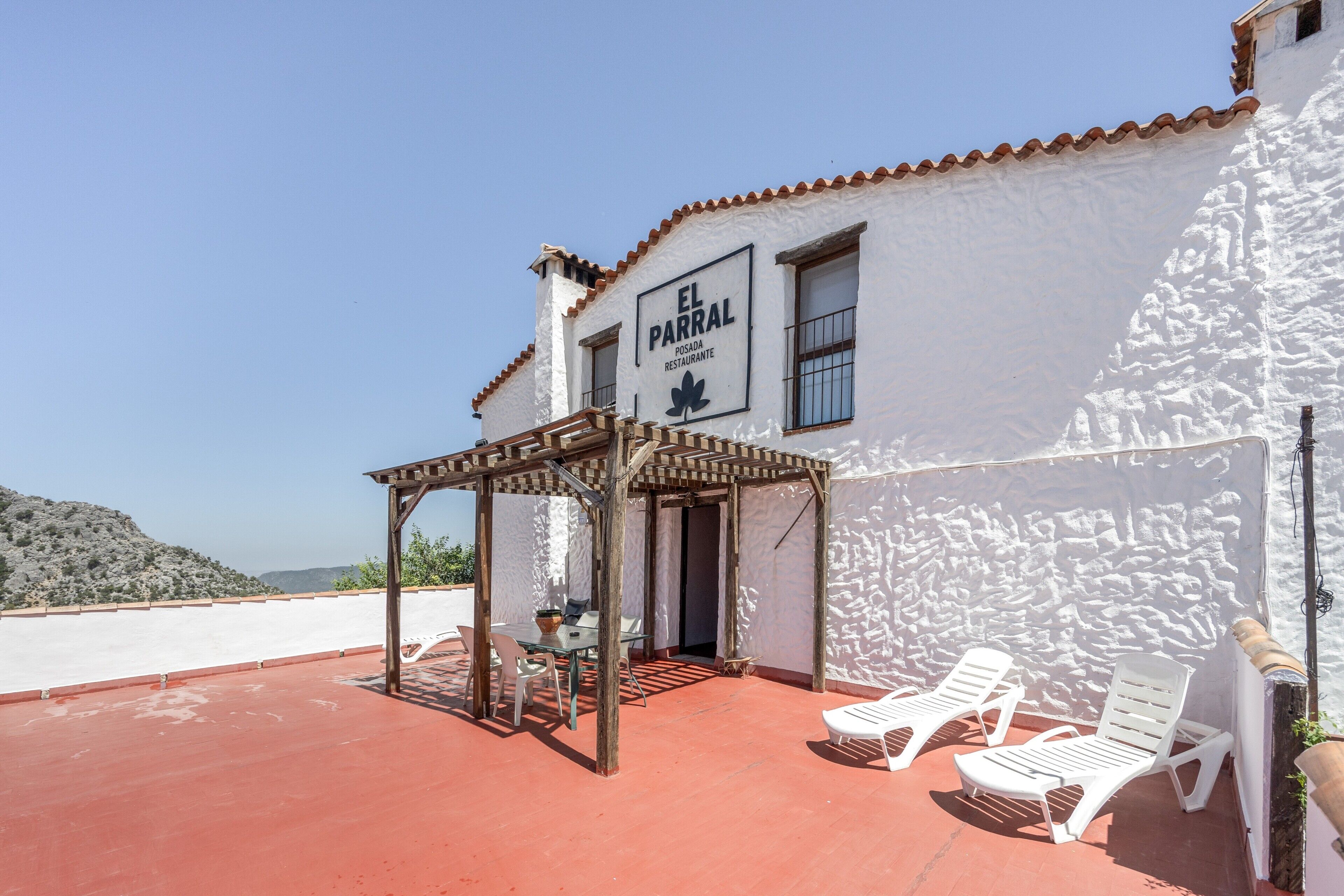 A white building with a sign reading 'EL PARRAL RESTAURANTE' and a covered outdoor seating area with lounge chairs.