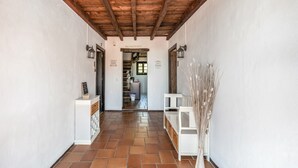 A hallway with a tiled floor, wooden ceiling beams, white walls, and a door leading to a kitchen area. - Hostal Posada El Parral – Private Pool and Restaurant in the Sierra de Cádiz (Benaocaz)