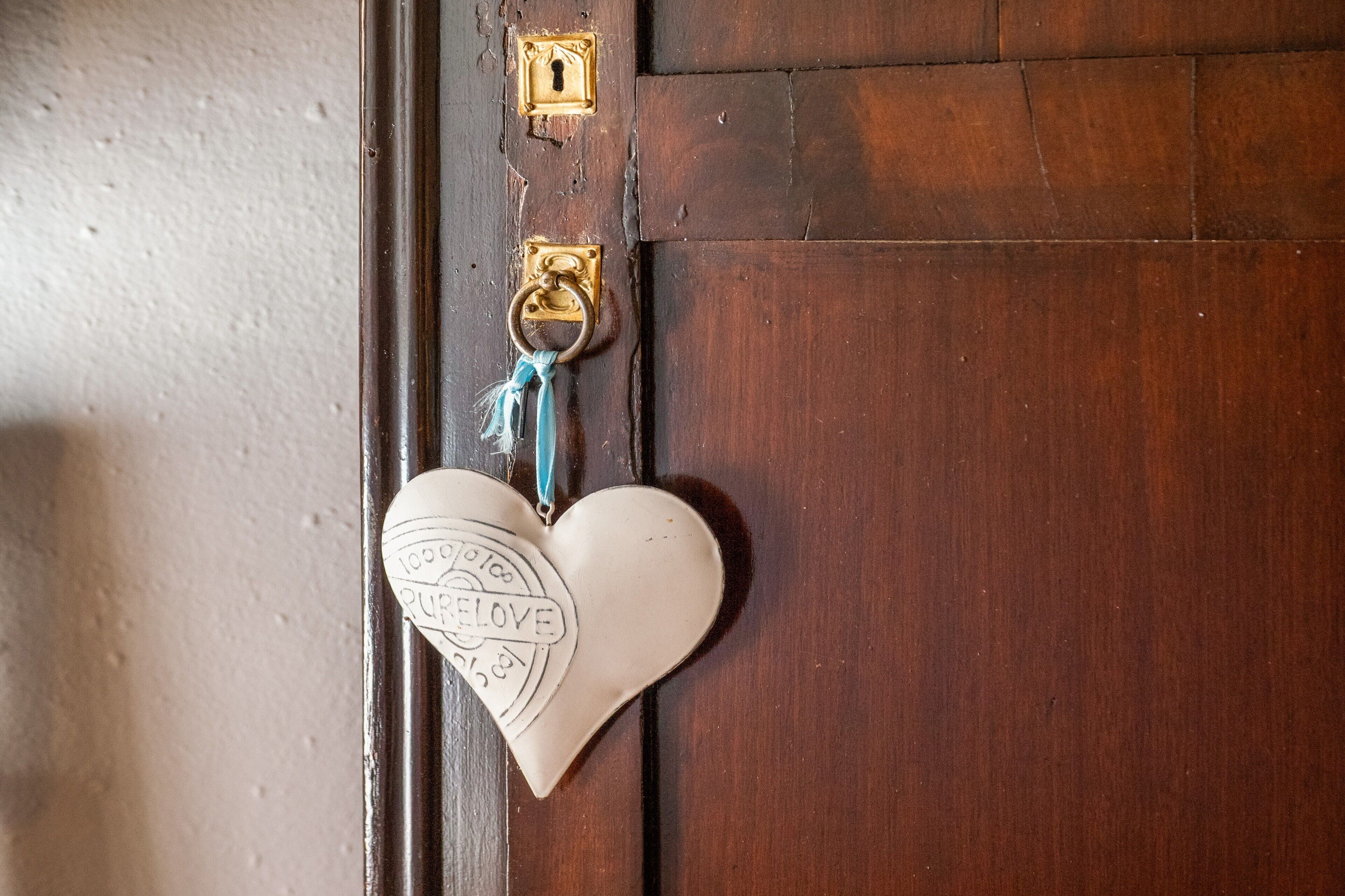 Une porte en bois avec une poignée de porte en laiton et un porte-clés en forme de cœur orné d’un cadenas.