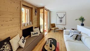 Uma sala de estar moderna com paredes de madeira, um sofá com almofadas decorativas, uma mesa de centro com uma garrafa e uma cabeça de veado emoldurada na parede.