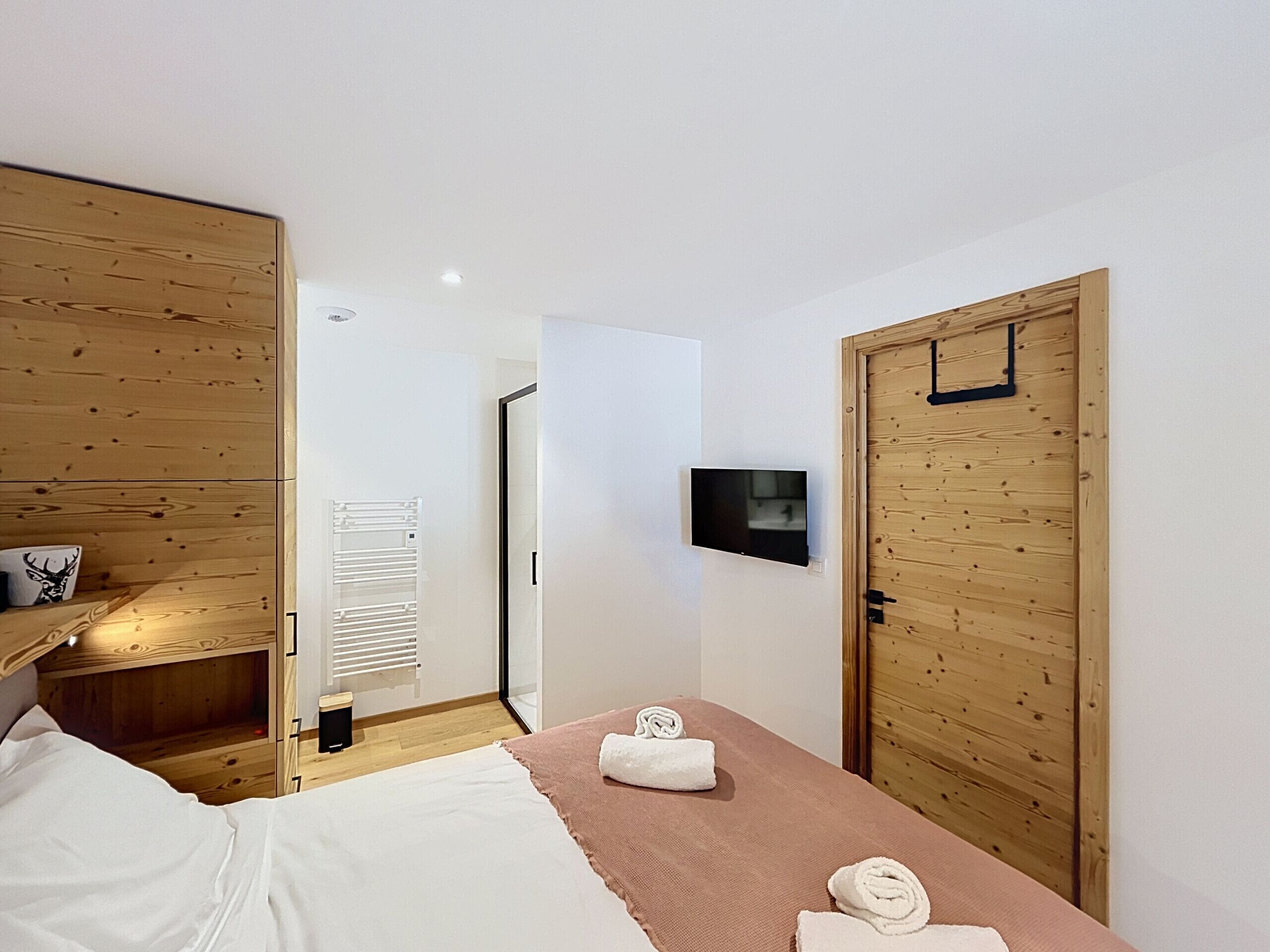 A bedroom with a bed, a TV mounted on the wall, and a wooden door.