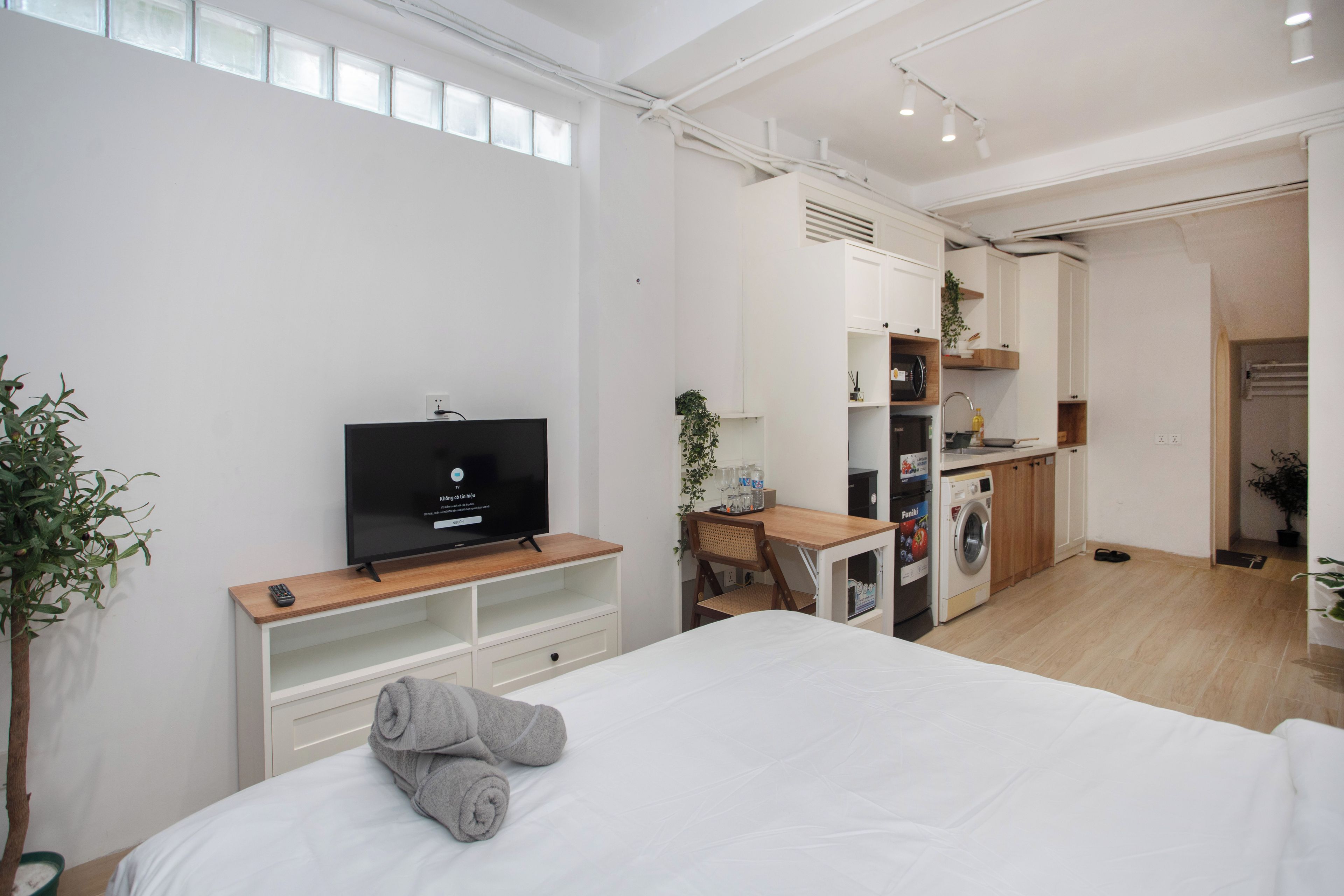 A modern bedroom with a TV, a desk, a chair, a bed, and a washing machine.