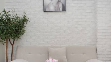 Una sala de estar con un sofá blanco, una mesa de centro blanca con un florero y un control remoto, además de una planta en maceta.