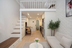 Een modern interieur met een trap naar een loft, een eethoek en een woonruimte met een bank en een plant.