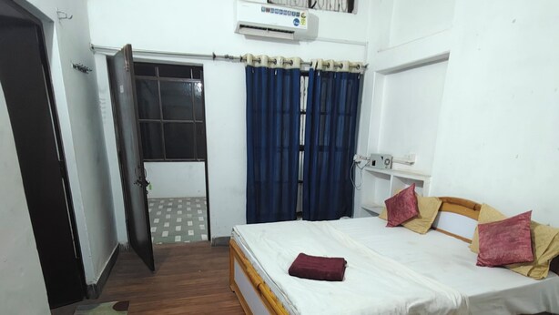 A bedroom with a bed, a desk with a keyboard and mouse, a window with curtains, and an air conditioning unit.