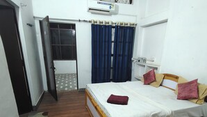 A bedroom with a bed, a desk, an air conditioning unit, and a window with curtains.