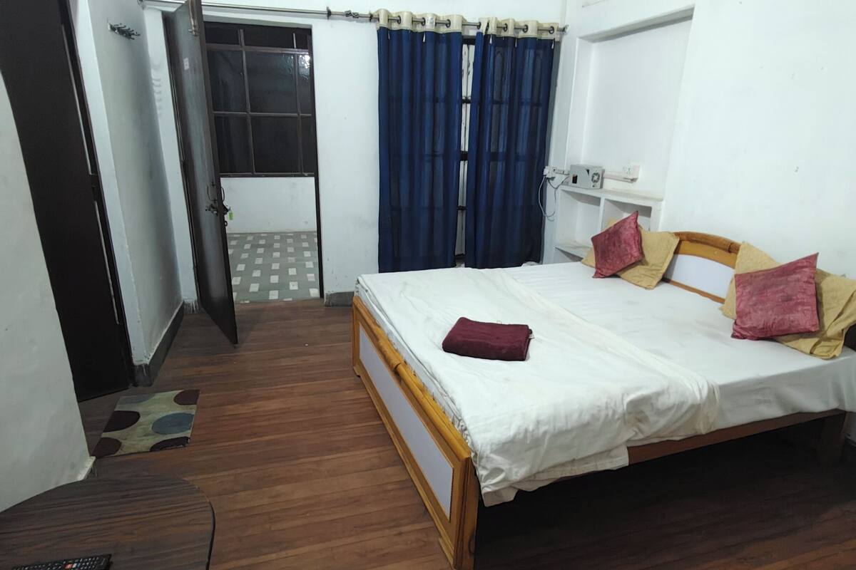 A bedroom with a bed, a desk, an air conditioning unit, and a window with curtains.