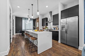 A modern kitchen with a central island, bar stools, stainless steel appliances, and a wooden floor. - New! Rooftop Views, Speakeasy + Karaoke, Sleeps 12 (Nashville)