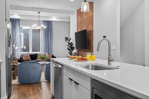 A modern kitchen with a built-in dishwasher, a stainless steel sink, and a flat-screen TV mounted on the wall. - New! Rooftop Views, Speakeasy + Karaoke, Sleeps 12 (Nashville)