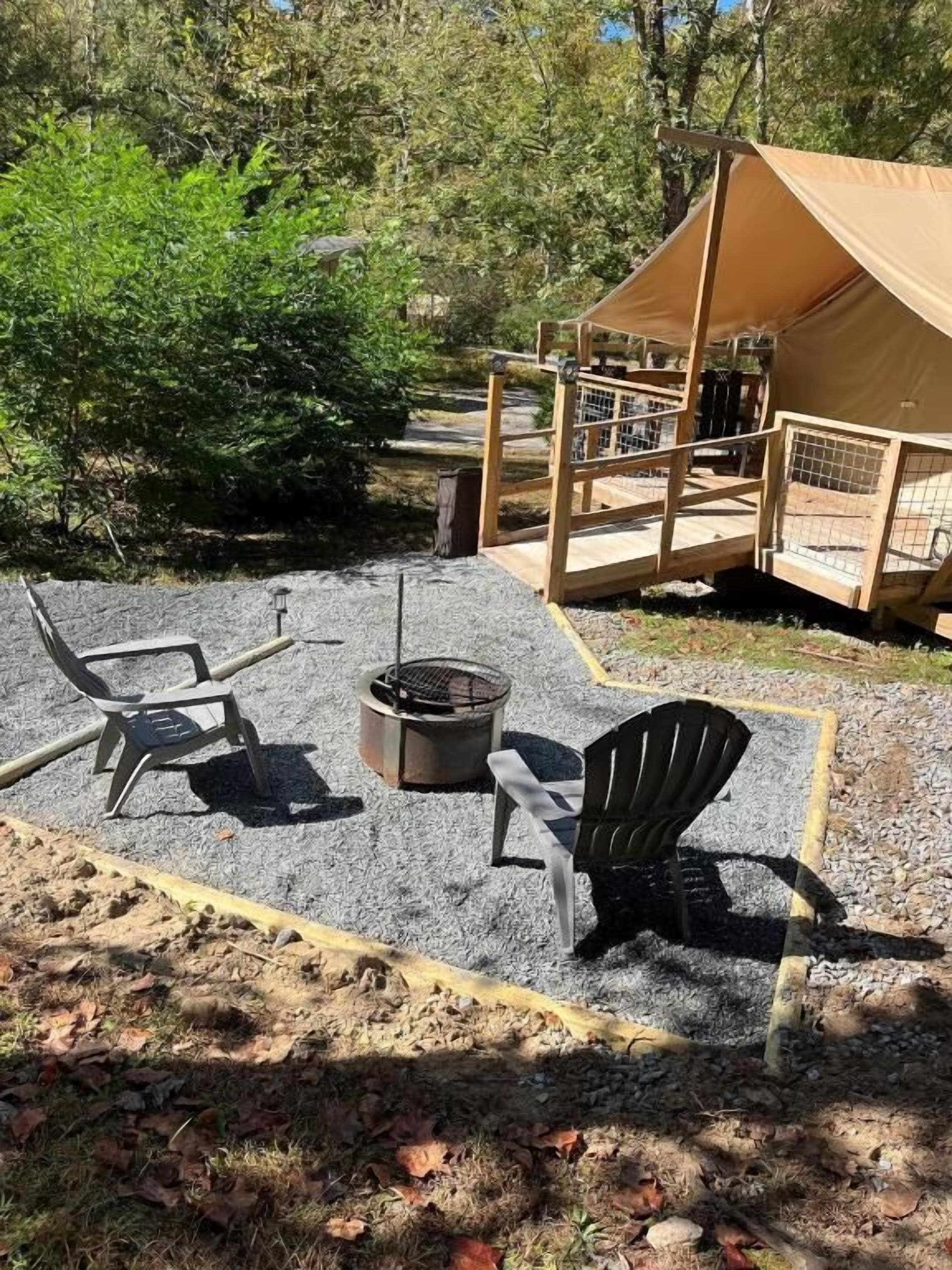 A tent with a fire pit and two Adirondack chairs in a forested area.