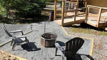 A tent with a fire pit and two Adirondack chairs in a forested area.
