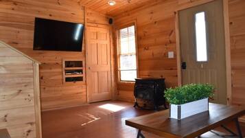 A wooden cabin interior with a television mounted on the wall, a fireplace, and a bench with a potted plant.
