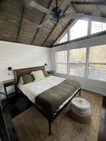 Un dormitorio con cama, ventilador de techo, ventana y vista al exterior.