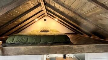 Un dormitorio tipo loft con techo inclinado, una cama litera y una pequeña zona de kitchenette.