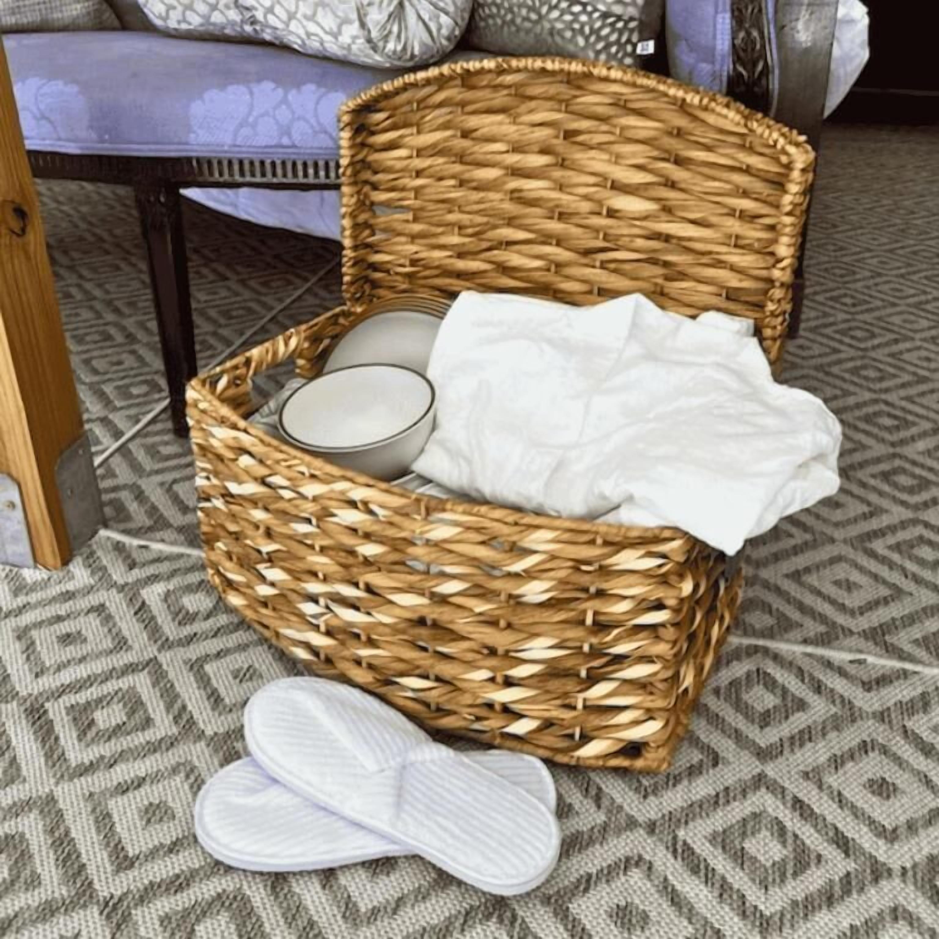A wicker basket with a white cloth and a pair of white slippers on a patterned floor.