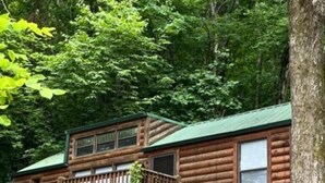A rustic cabin with a wooden deck and a staircase leading to the entrance.