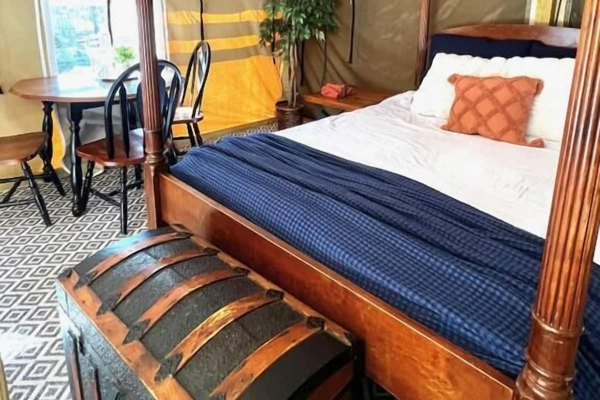Una cama con dosel con un edredón azul, un banco de madera con respaldo curvo y un suelo estampado.