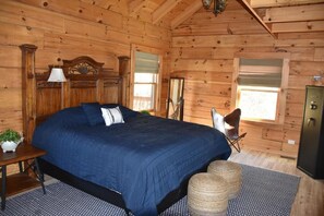A wooden cabin bedroom with a large bed, a nightstand, a chair, and a wardrobe. - Wilderness Cove Campground (Saluda)