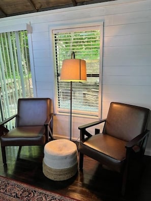 A room with two leather chairs, a woven ottoman, a floor lamp, and a window with blinds. - Wilderness Cove Campground (Saluda)