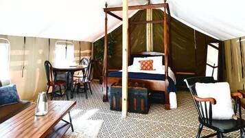 Un hébergement sous tente doté d’un lit à baldaquin en bois, d’une table à manger, de chaises et d’un sol à motifs.