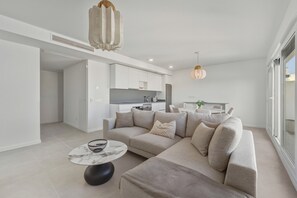 A modern living room with a sofa, a round coffee table, and a kitchen in the background. - 3025 Elegant apartment with terrace and pool (Estepona)