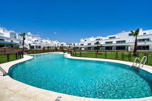 A swimming pool with a clear blue water, surrounded by white buildings and palm trees. - 3025 Elegant apartment with terrace and pool (Estepona)