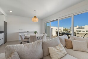 A modern apartment with a dining area, a sofa, and a large window offering a city view. - 3025 Elegant apartment with terrace and pool (Estepona)