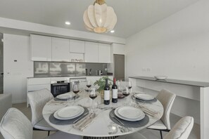 A modern dining area with a round table set for six, white cabinets, a kitchen in the background, and a pendant light above the table. - 3025 Elegant apartment with terrace and pool (Estepona)