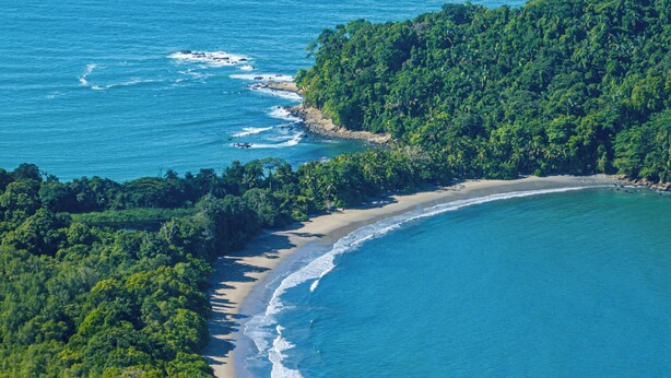 An aerial view of a coastal area with dense greenery, a sandy beach, and clear blue waters. - Casa Infinity | Hilltop Ocean-View | 42' Infinity Pool | Near Manuel Antonio (Portalon)