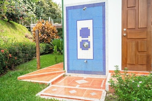 A tiled wall with a door, a small garden with grass and flowers, and a wooden door. - Casa Infinity | Hilltop Ocean-View | 42' Infinity Pool | Near Manuel Antonio (Portalon)