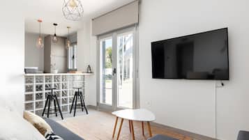 Ein modernes Wohnzimmer mit Fernseher, Sitzgelegenheiten und einer Küchenzeile mit Barhocker.