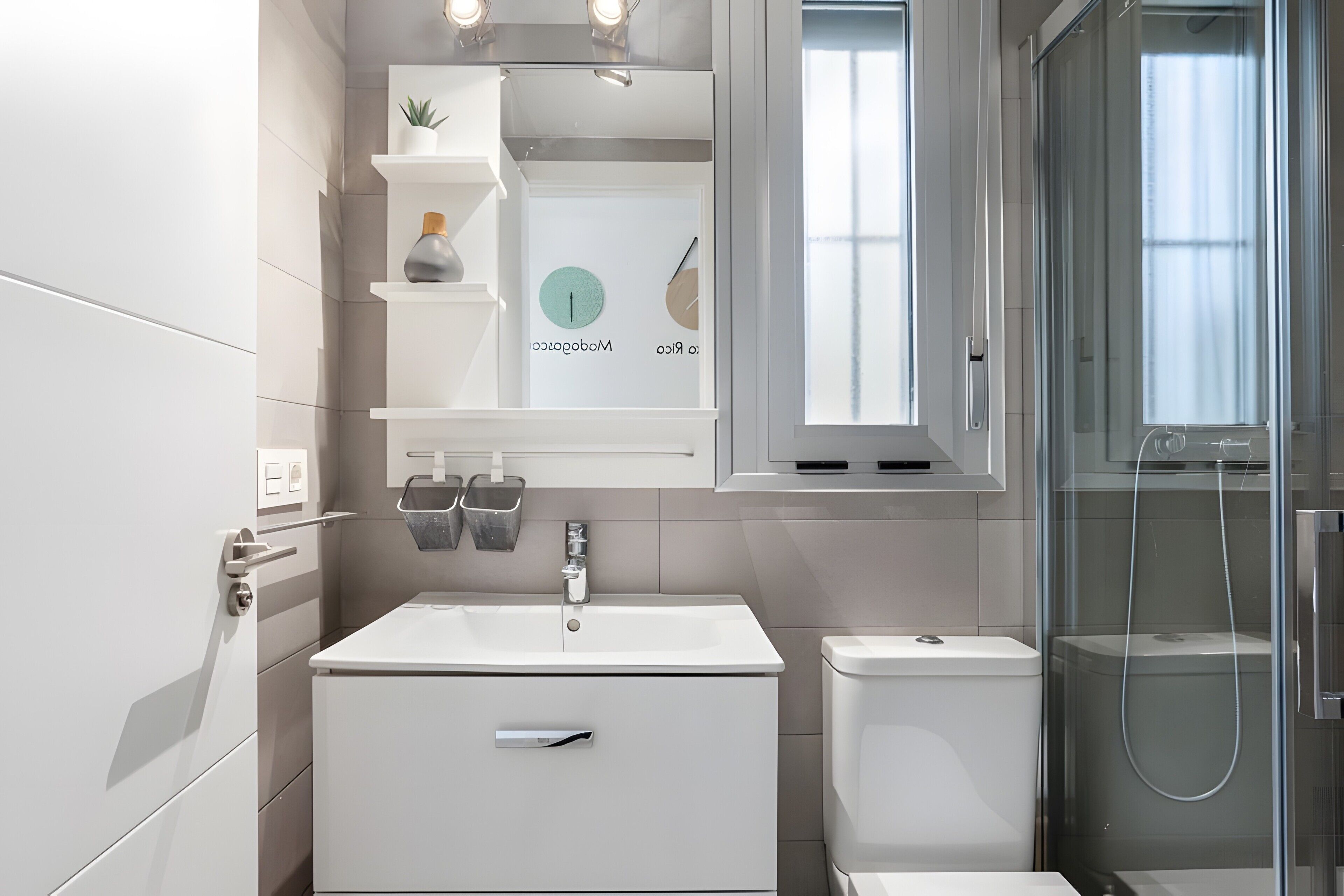 A modern bathroom with a white sink, toilet, and shower. There are shelves with toiletries and a mirror above the sink.