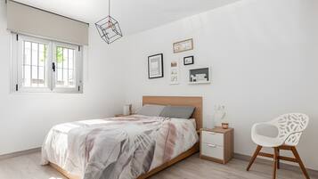 Ein Schlafzimmer mit einem Bett, Nachttischen, einem Sessel und Wandbildern.