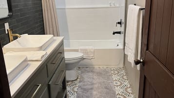 A bathroom with a double sink, toilet, bathtub, and a shower curtain.